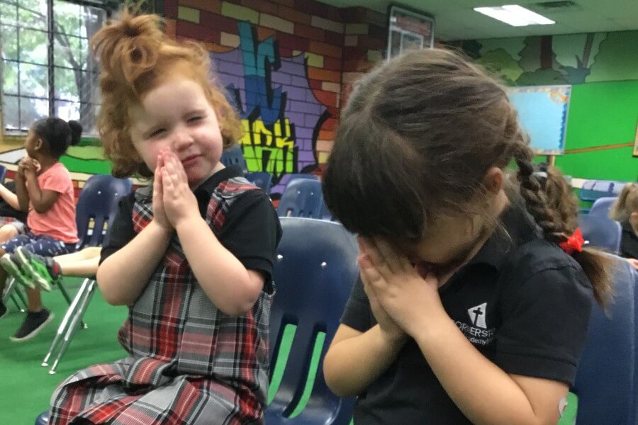 two young girls praying at school